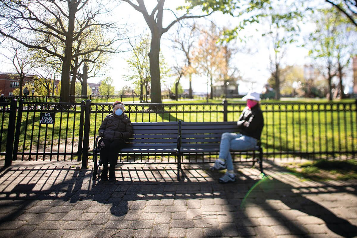 A picture of two people socially distancing on a park bench in Federal Hill by sitting far apart from eachother.
